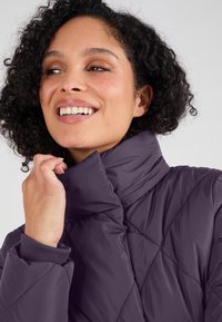Lila gewatteerde pufferjack met een hoge kraag. Heeft een gladde textuur en elastische manchetten, wat warmte en comfort biedt in koude weersomstandigheden.