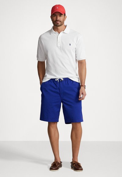 White polo shirt, blue shorts with drawstring, and red cap. Brown boat shoes with laces. Simple design with classic logo accents.
