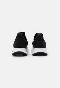 Sorte atletiske sko med en tekstureret stofoverdel, hvid mellemsål, sort sål og med en diskret guldaccent på hælen.