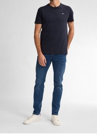 Námorně modré bavlněné tričko s krátkým rukávem a kulatým výstřihem, doplněné modrými džínami a bílými teniskami.