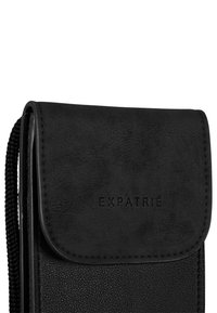 Černá pouzdro na telefon z umělé kůže s klopovým uzavřením, strukturovaným povrchem, vyraženým logem a tkaným popruhem pro nošení.