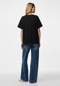 Svart oversize t-shirt med korta ärmar, kombinerad med högmidjade, vida jeans i denim. Tyget ser slätt och mjukt ut.