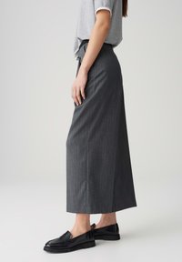 Grijze pinstriped broek met een wijdere pijp en een licht gestructureerde stof. Gepaard met zwarte gepatineerde instappers.