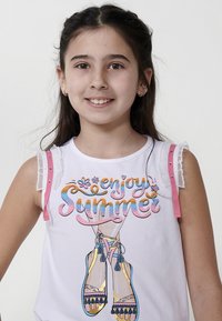 Bijela majica bez rukava s šarenim natpisom "uživaj u ljetu", ružičastim trakama i volanastim čipkastim detaljima. Sadrži grafiku sandala s resicama.