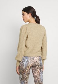 Beige gebreide trui met opstaande mouwen en een geribbelde textuur. Gecombineerd met slangenprint leggings in tinten bruin, grijs en crèmekleurig.