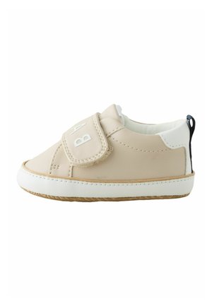 Zapato para niño pequeño en beige y blanco con parte superior de cuero suave, correa de Velcro, puntera redonda y suela de goma con costura decorativa en relieve.