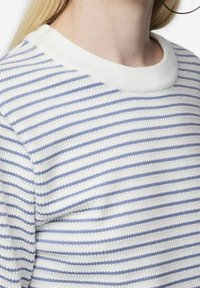 Biały sweter z cienkimi niebieskimi paskami, prążkowanym kołnierzem oraz teksturowanym materiałem z subtelnym wzorem. Zbliżenie na dekolt i ramię.