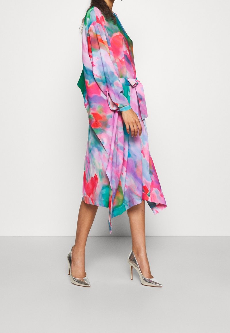 Vestido fluido con un patrón abstracto en acuarela en tonos rosa, azul y verde, combinado con zapatos de tacón alto metálicos.