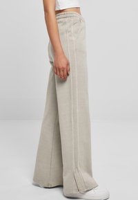 Lichtgrijze wijde broek met een elastische tailleband, zijstiksels en een iets uitlopende zoom. Gepaarde met witte sneakers.