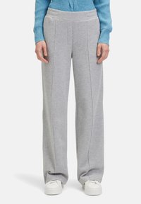 Lichtgrijze joggingbroek met een wijd uitlopende snit, gekenmerkt door verticale naaien en een zachte textuur. Gecombineerd met witte sneakers.