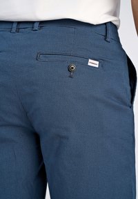 Pantaloni blu con motivo, realizzati in un tessuto testurizzato, dotati di tasche frontali, chiusura con bottone e un'etichetta sulla vita.