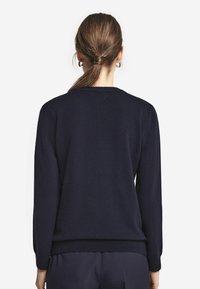 Granatowy sweter z okrągłym dekoltem, długimi rękawami oraz prążkowanymi mankietami i dołem. Gładka faktura bez wzorów lub ozdób.