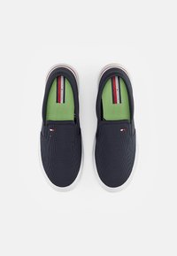 Námořnické slip-on boty s texturovanou tkaninou, bílou gumovou podrážkou a zelenými vnitřními vložkami. Obsahují logo Tommy Hilfiger na straně a pruhované akcenty.