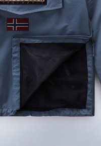 Blauwe jas met een Noorwegen vlag patch, een ritszak met meshvoering en een gladde buitenstof.