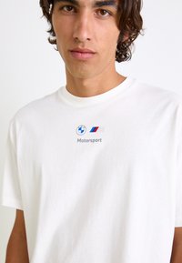 Hvid bomulds t-shirt med rund halsudskæring og korte ærmer, med BMW Motorsport logo og tekst på brystniveau.