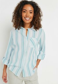 Camicia a maniche lunghe a righe blu chiaro e bianche con colletto button-down e tasca sul petto; tessuto strutturato con maniche arrotolate.