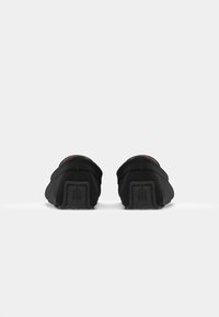 Svarta slip-on-skor med ett slätt tygövre och ett texturerat gummisulor, med en rundad häl och minimalistisk design.