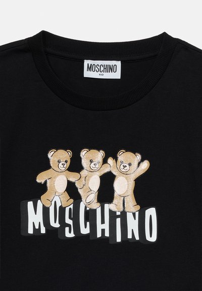 Μαύρο μπλουζάκι με τρεις ταμπελί τενεκεδένιες αρκούδες πάνω από το λευκό κείμενο "MOSCHINO" και μια λευκή ετικέτα λαιμού που γράφει "MOSCHINO KID."
