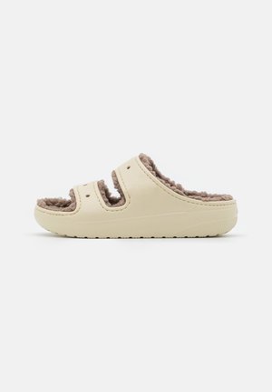 Pantofole slip-on color crema con un interno testurizzato e soffice. Presentano due cinghie con ritagli e una suola in gomma con fondo decorato.