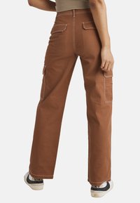 Brune cargo-bukser med bred ben-design, hvide sømme, to baglommer og en sidelomme. Bæret med hvide og sorte sneakers.