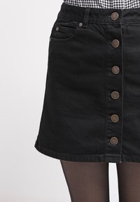 Svart denimkjol med rak skärning, framknappar och två sidofickor. Mjuk textur och medellängd.