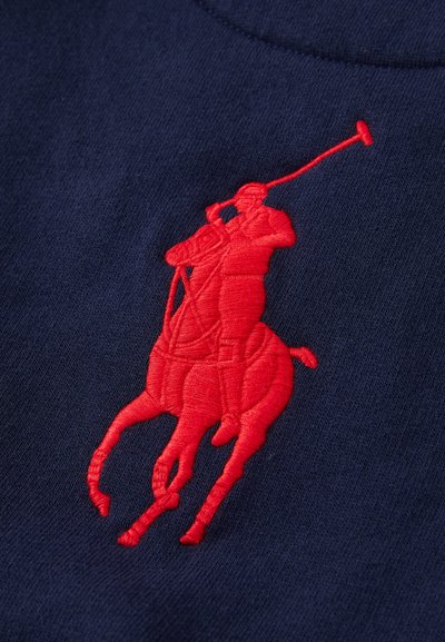 Jūros mėlynumo audinys turi didelį raudoną siuvinėtą polo žaidėjo ir arklių dizainą, išryškinantį smulkų siuvimą ir glotnų paviršių.