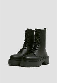 Stivali alla caviglia in pelle nera con suola platform spessa, allacciatura frontale e zip laterale. Superficie texturizzata con finitura liscia.