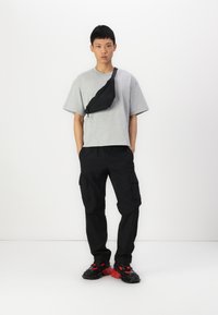 Grå oversized T-shirt, sorte cargo bukser med sidelommer, og kraftige sorte sneakers med røde accenter; en sort crossbody taske båret diagonalt.
