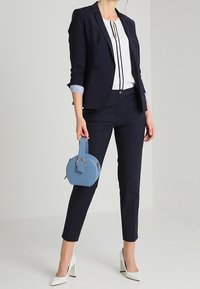 Blazer azul marino sobre una blusa blanca con rayas verticales negras, combinado con pantalones ajustados azul marino. Los accesorios incluyen un pequeño bolso redondo azul y tacones blancos.