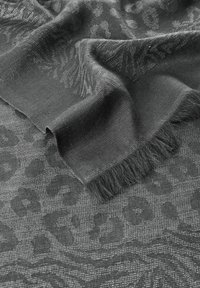 Tissu texturé gris avec motif léopard et bords effilochés, présentant une finition douce et tissée qui capte la lumière.