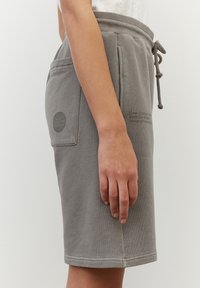 Shorts en coton gris avec taille à cordon, poche latérale et détail logo. Texture lisse et coupe jusqu'aux genoux.