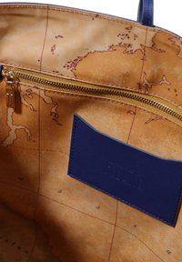 Interno in tessuto marrone con una stampa mappamondo, un'etichetta in pelle blu sul lato e una cerniera dorata lungo il bordo superiore.