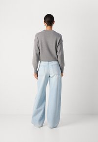Suéter de punto gris con cuello de canalé y hombros caídos, combinado con jeans de pierna ancha azul claro que cuentan con bolsillos traseros y costuras sutiles.