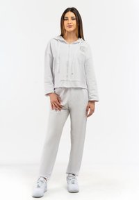 Svetlosivý skrátený hoodie s predným zipsom, dvomi prednými vreckami a šnúrkami, kombinovaný s rovnakými sivými teplákmi. Biele tenisky.