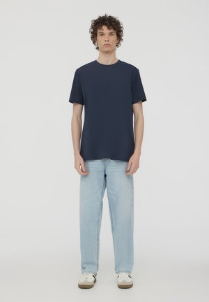 Granatowa bawełniana koszulka z krótkim rękawem i okrągłym dekoltem, w połączeniu z jasnoniebieskimi dżinsami i białymi sneakersami z brązowymi akcentami.