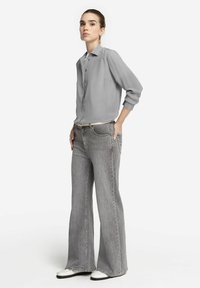 Graue Bluse mit Knopfleiste und langen Ärmeln, kombiniert mit grauen weit geschnittenen Jeans und weißen Schuhen. Einfaches, klares Design ohne Muster.