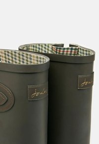 Tumed rohelised kummisaapad, mille siseküljel on pluusikangast vooder ja ülaosas on nahast plaastrid, millele on peale pressitud "joules".