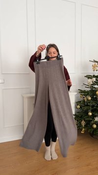 Light grey, wide-leg pants made from knitted material, displayed on a hanger, featuring a ribbed waistband, held by a person indoors.