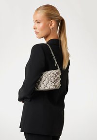 Sac argenté matelassé avec chaîne, présentant une surface texturée et des nœuds décoratifs. Posé sur un blazer noir.