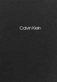 Czarna bawełniana koszulka z okrągłym dekoltem, miękką fakturą i białym haftowanym logo "Calvin Klein" na środku.