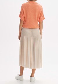 Perzikkleurige gebreide trui met korte mouwen boven een geplooide, lichtbeige rok. Draag het met witte sneakers, wat een ontspannen silhouet laat zien.