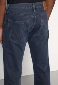Mörkblå denimjeans med rak passform, utrustade med två bakfickor med distinkt sömnad och en lädermärkestagg på midjebandet.