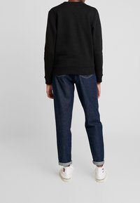 Černá mikina s kulatým výstřihem, žebrovanými manžetami a lemem, spárovaná s volně střiženými tmavě modrými džíny a bílými teniskami. Neformální, univerzální vzhled.