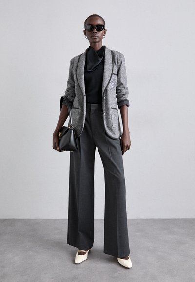 Blazer à carreaux gris avec bord noir, haut ajusté noir, large pantalon gris et chaussures à bout pointu crème. Sac à main noir et lunettes de soleil inclus.