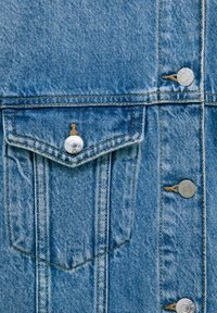 Veste en denim bleu clair avec une poche poitrine, des boutons-pression argentés et un tissu texturé avec des détails de coutures visibles.