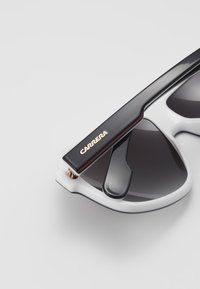 Sunglasses with a white frame, black temples, and gradient dark lenses. Features gold "Carrera" branding on the temple.