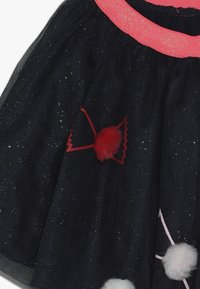 Czarna, błyszcząca spódnica z tiulu z różowym pasem, udekorowana czerwonymi i białymi pomponami przymocowanymi cienkimi sznurkami.