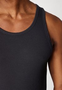 Black ribbed tank top with a rounded neckline, featuring a close-fitting design that highlights the neckline and armholes.
