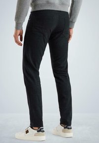 Pantalones elásticos negros de corte ajustado, con bolsillos traseros y una textura suave, combinados con zapatillas de color claro.