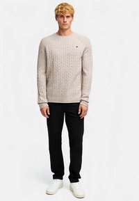 Kermansävyinen neulepaita punottuine kuvioineen, pyöreällä pääntiellä ja resorinauhalla varustettuine hihoineen, yhdistettynä mustiin housuihin ja valkoisiin lenkkareihin.